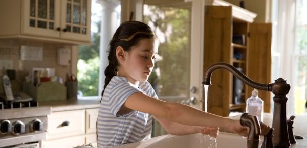 Young girl turning on the kitchen faucet