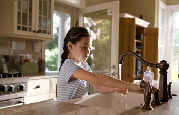 Young girl turning on the kitchen faucet